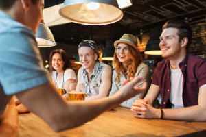 people, leisure, friendship and communication concept - group of happy smiling friends drinking beer and talking at bar or pub